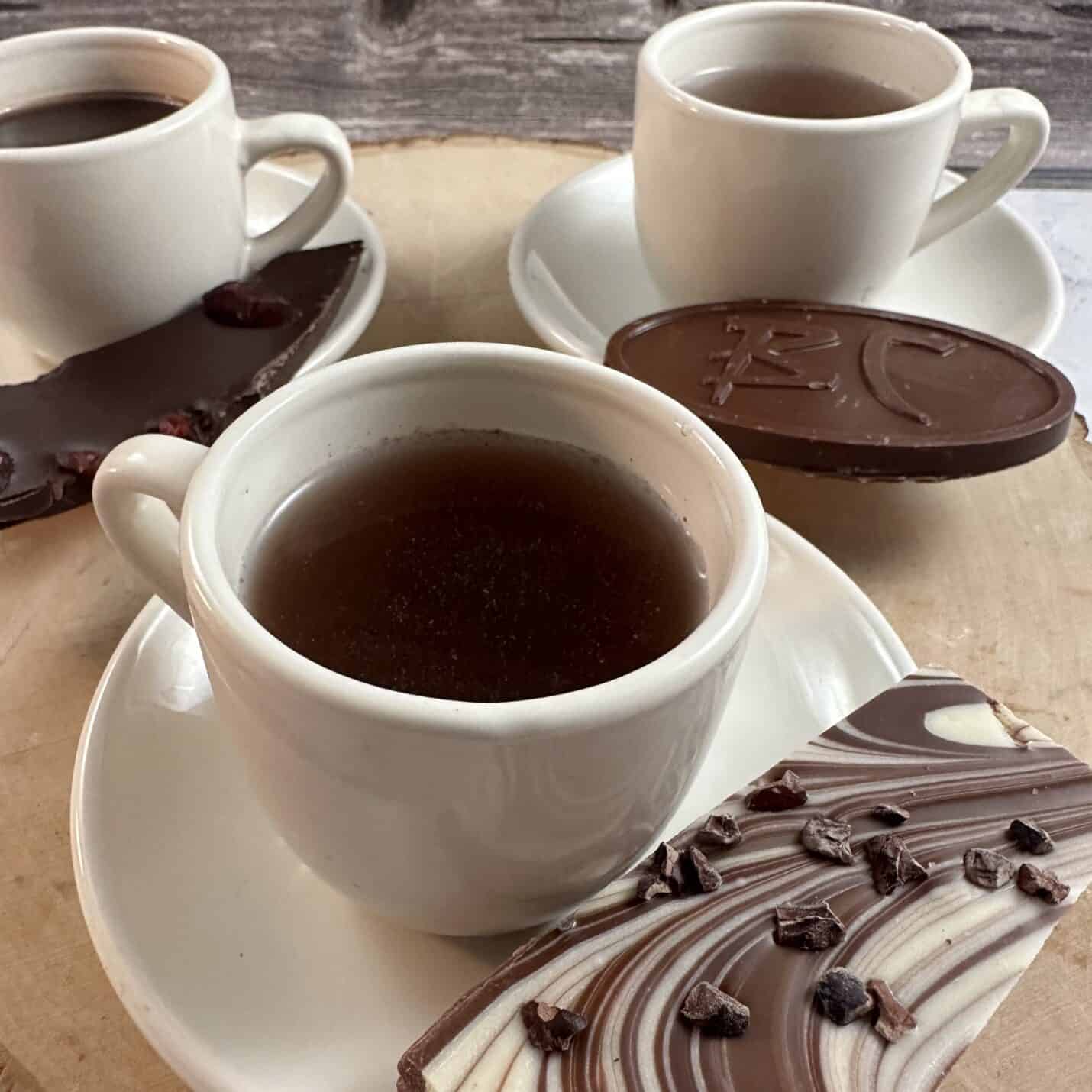 Three small cups of chocolate drinks with three pieces of chocolate